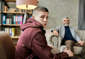 a teen boy looks sad in front of a therapist during adolescent alcohol addiction treatment 