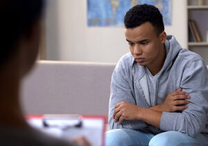 a teen boy thinks while a therapist takes notes during somatic therapy 