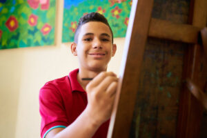 a boy smiles while painting in art therapy for teens