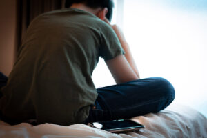 a teen sits on a bed holding his head, one of the signs of a panic disorder