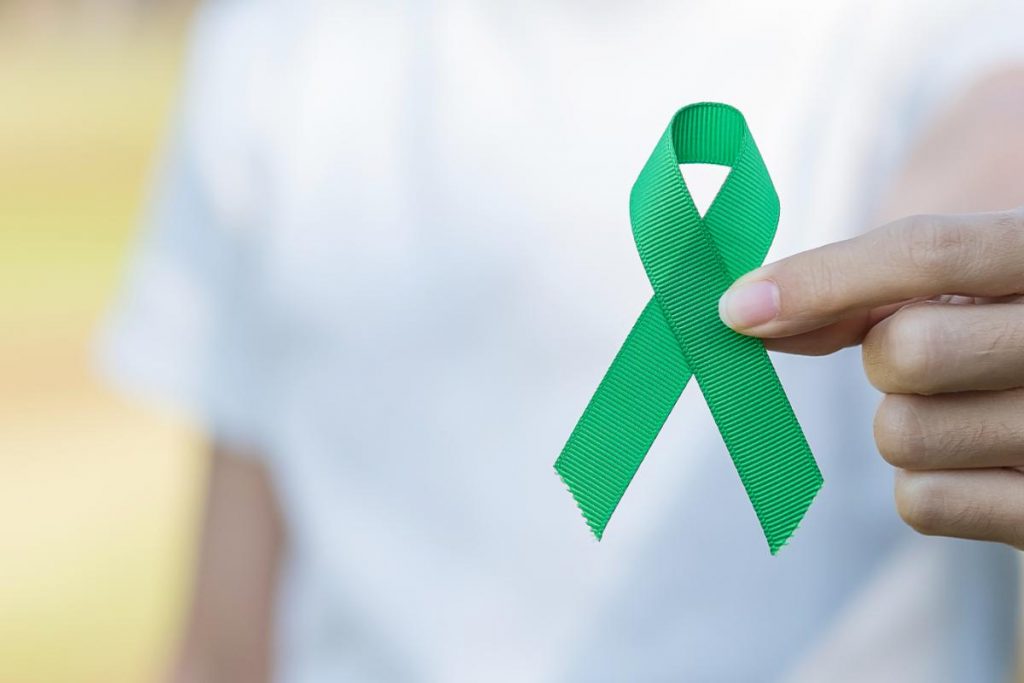 Person handing out a green ribbon because May is Mental Health Awareness Month