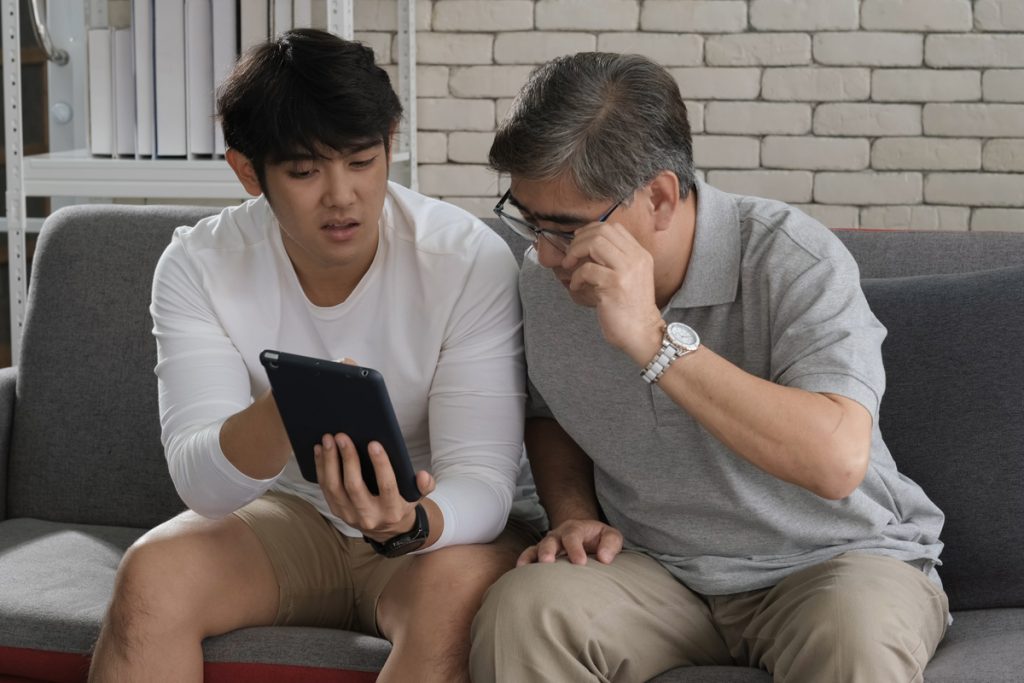 Father looking at teen son's tablet