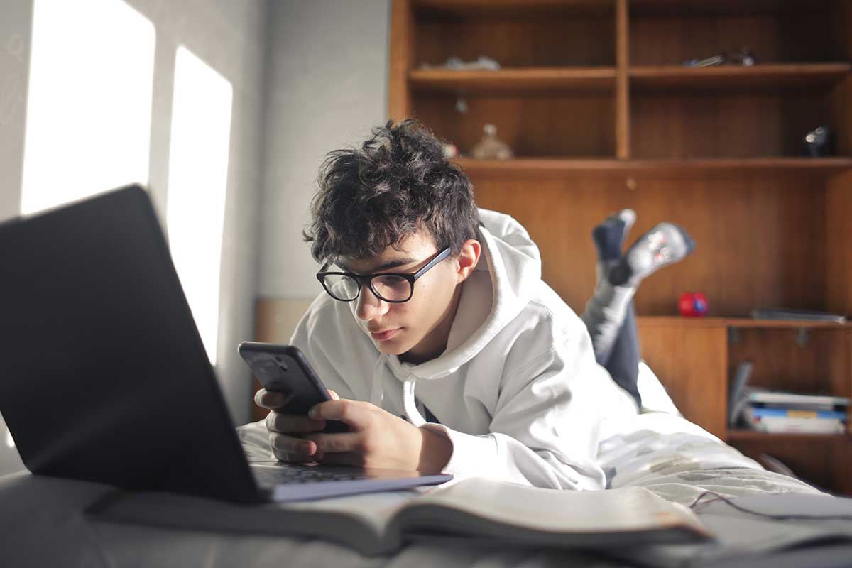 a teen sits on their phone while doing homework, possibly dealing with negative effects of social media