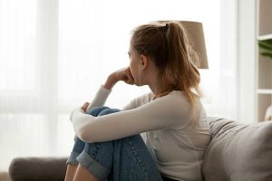 a young person sits on a couch thinking, possibly about the relationship between ptsd and tics