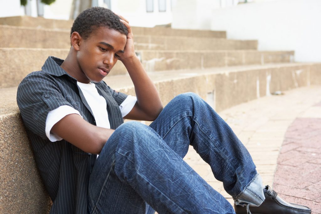 a teen looks sad sitting on steps, perhaps needing a trauma assessment