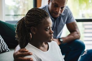 Father comforting his teenage daughter as she looks away thoughtfully.
